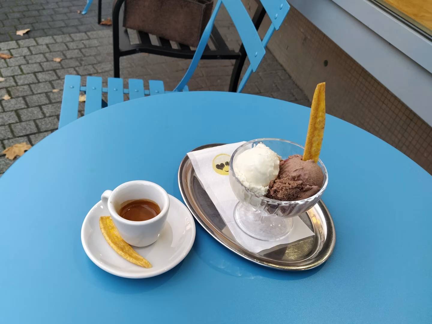 Ein Espresso und ein Eisbecher auf einem Tisch. Neben dem Espresso liegt ein gelber Bananenstick. Im Eis steckt ein Bananenstick.